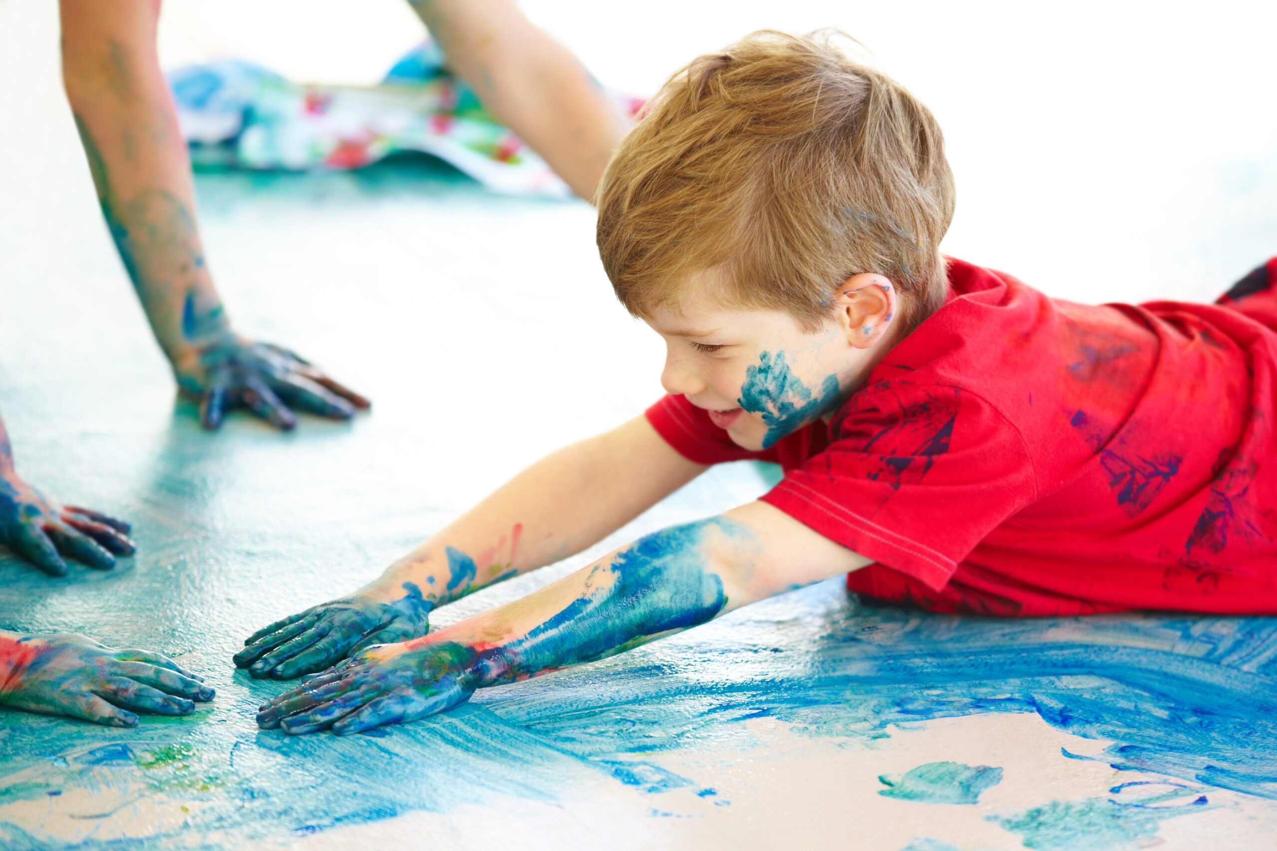 Cute little boys using fingerpaint on the floor.